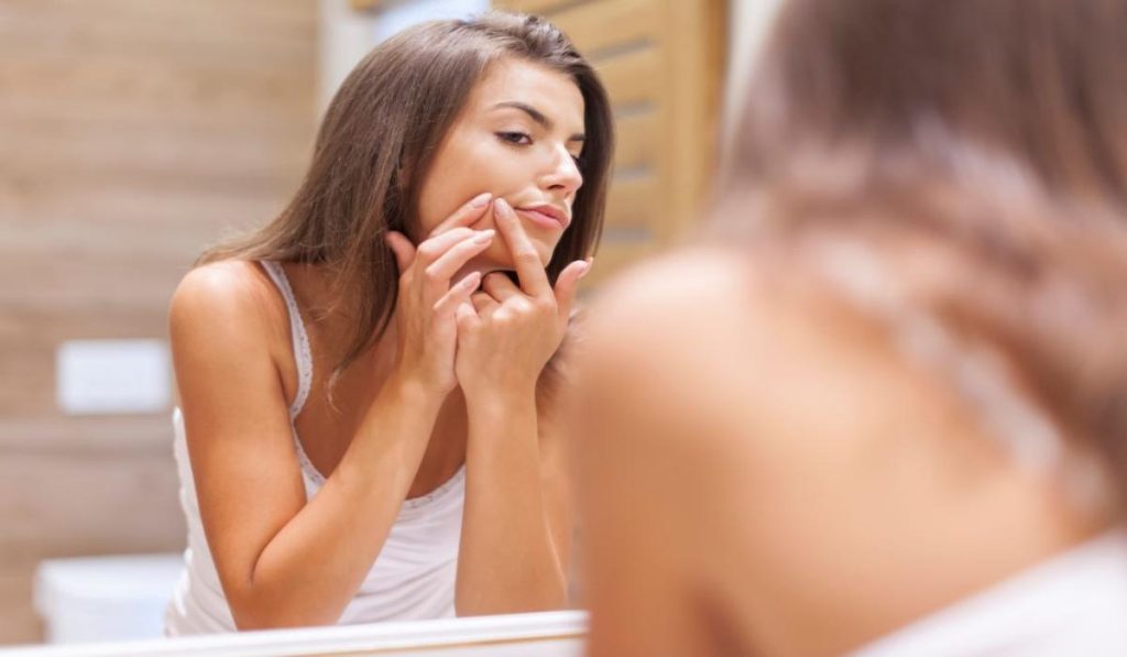Primer plano de chica mirandose al espejo la irritación tras depilación con cera en la zona del labio superior