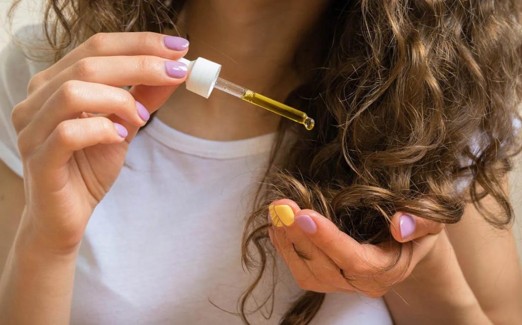 Mujer aplicando sérum en cabello con mechas.