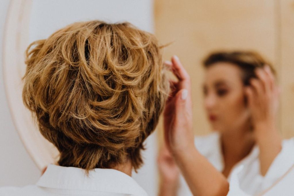 Mujer observando su cabello frente al espejo preocupada por la caída del cabello.