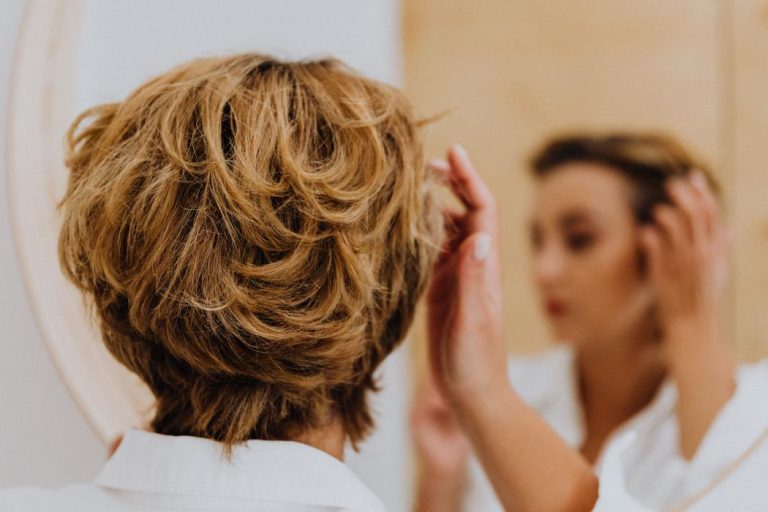 Mujer observando su cabello frente al espejo preocupada por la caída del cabello.