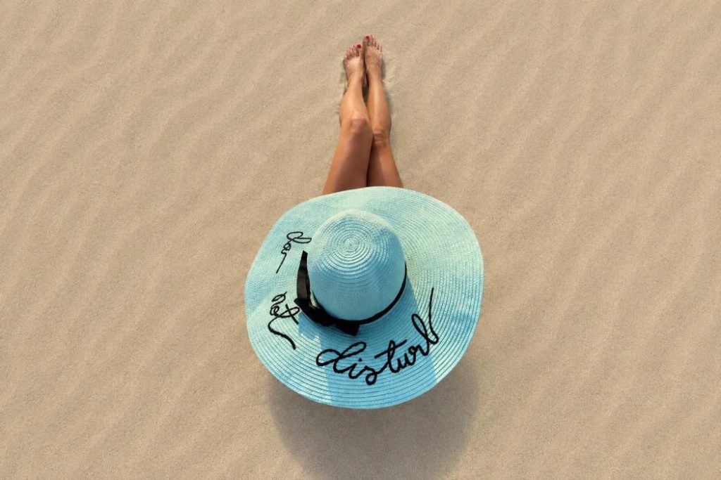 Mujer descansando en la playa con sombrero de ala ancha para ilustrar un artículo sobre si caduca el protector solar y los mitos de la protección solar.