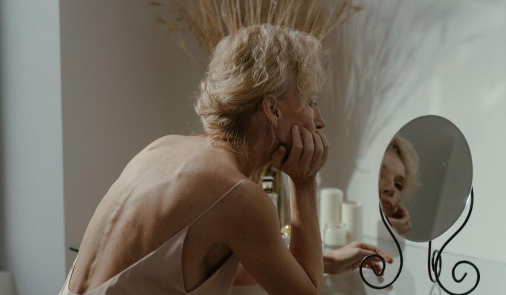 Mujer observando su rostro en el espejo antes de elegir un tratamiento facial