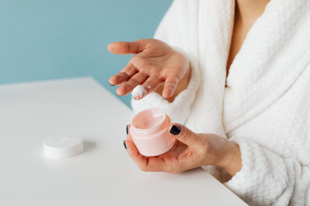 Mano con una pequeña cantidad de crema facial en el dedo y un tarro abierto