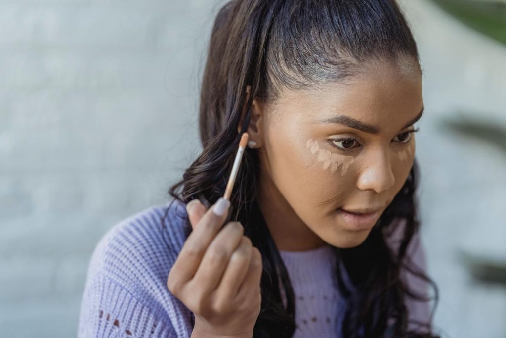 Mujer con puntos de corrector bajo ambos ojos sosteniendo el aplicador.